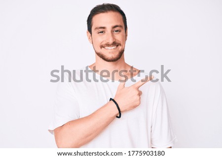 Young handsome man wearing casual white tshirt cheerful with a smile of face pointing with hand and finger up to the side with happy and natural expression on face 