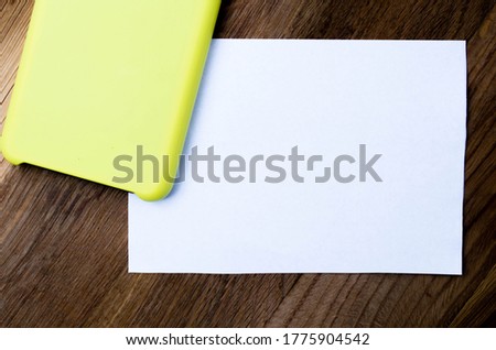 Black smartphone in a yellow case on a wooden background near a white sheet Mock up. Smartphone and white sheet of paper Mock up