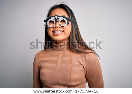 Young asian optical girl controlling eyesight using optometry glasses over white background with a happy and cool smile on face. Lucky person.