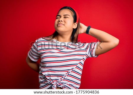 Young beautiful asian girl wearing casual striped t-shirt over isolated red background Suffering of neck ache injury, touching neck with hand, muscular pain