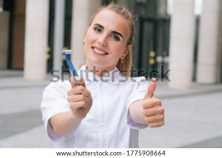 Beautician young girl holds a razor, the doctor woman with a smile shows her finger up