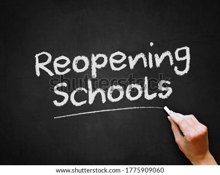 A hand writing 'Reopening Schools' on chalk board for schools reopening plans after Covid-19 (Coronavirus) pandemic lockdown. Royalty-Free Stock Photo #1775909060