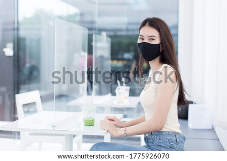 woman sitting in restaurant with table shield to protect infection from coronavirus covid-19, restaurant and social distancing concept. New normal.