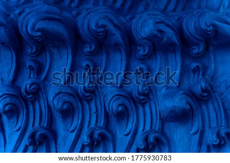 A bas-relief element in the form of sea waves at the base of the Buddha statue in a Buddhist temple. Abstract Indigo background. Blue Ocean waves.