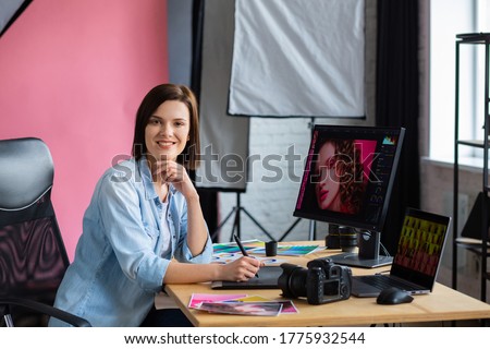 Portrait of graphic designer working in office with laptop,monitor,graphic drawing tablet and color palette.Retouching images in special program.Retoucher workplace in photo studio.Creative agency.