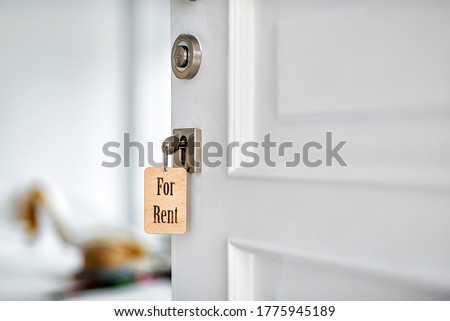 Key with wooden trinket in the door lock. The door is half open. Blurred background. Real estate for rent.