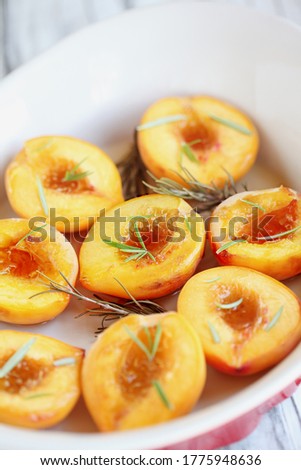 Fresh homemade roasted peaches baked in brown sugar and fresh rosemary sprigs. Selective focus with blurred foreground and background.