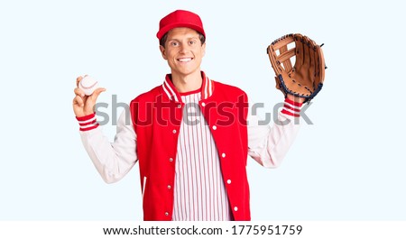 Young handsome man wearing baseball uniform holding golve and ball looking positive and happy standing and smiling with a confident smile showing teeth 