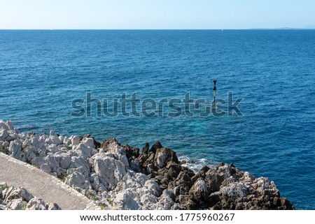 Rocky shore of Mediterranean Sea. Sign in the blue water. Saint Jean Cap Ferrat hiking trail, French Riviera. 