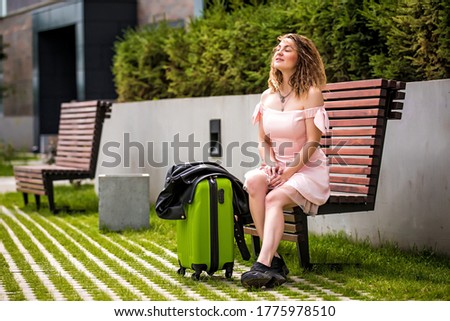 girl with a suitcase on the street. Girl with a suitcase goes on vacation. Girl with a suitcase travels. Girl with a suitcase sits on a bench