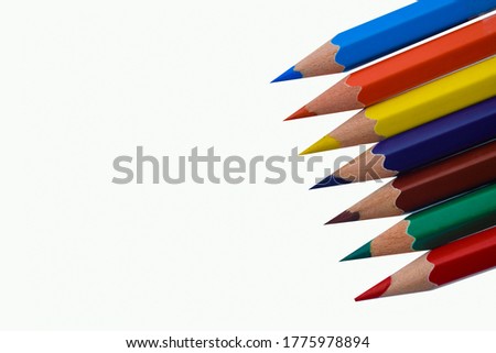 A row of seven different colored wood pencil crayon places on a white paper background