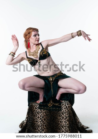 slim beautiful woman in decorated traditional green belly costume with top and skirt dancing on pedestal with leopard print on white background with copy space 