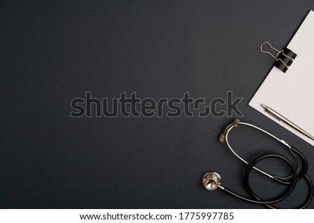 Medicine accessory, stethoscope with notepad, black background with copy space. top view