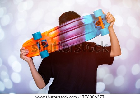 young boy holding colorful skateboard in hand and bokeh lights background