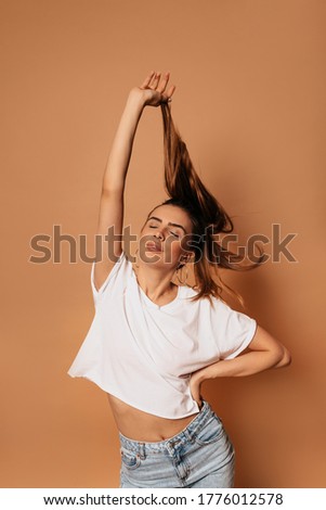spectacular beautiful female model posing with smile and closed eyes and playing with her hair over isolated beige background 