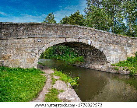 Sandstone Bridge 23 on a quiet, rural section of the Leeds to Liverpool Canal in Lancashire, UK. Taken on a sunny day with blue sky and white clouds in summer.
