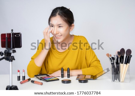 Asia woman beauty blogger does make up, reviews beauty product for video blog, gives advice to girls and women, films process on camera. Fashionable woman has online translation at home