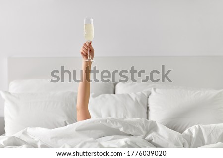 alcohol, celebration and morning concept - hand of young woman lying in bed with champagne glass Royalty-Free Stock Photo #1776039020