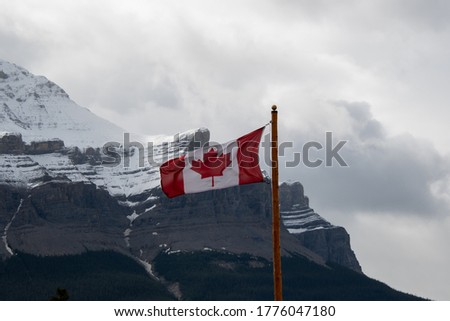 A picture of Canada flag waving against Mount Murchison.   