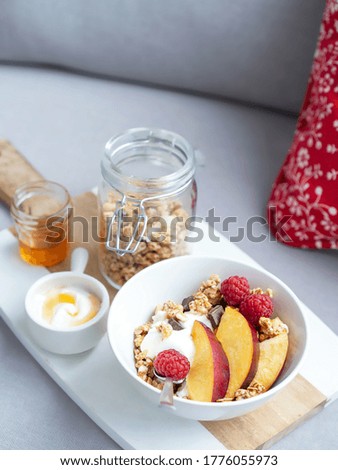 Bowl of homemade granola with yogurt, honey, fresh raspberries and nectarines on a sofa. Stay at Home Healthy Breakfast. Selective focus, space for text.