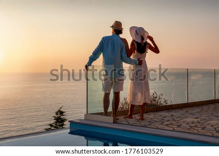 A romantic couple with hats on vacation time enjoys the summer sunset by the pool Royalty-Free Stock Photo #1776103529