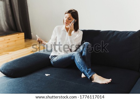 young girl sitting sofa home holding hand medicine tablets talking on phone court glass of water brunette one