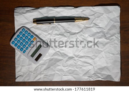 pen, a sheet of paper and a calculator on a wooden table