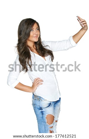 Happy young girl taking pictures of herself through cellphone, over white background