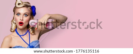 Portrait image - amazed shocked or very happy excited woman with phone. Pin up girl, keeping mouth open - unbelievable sales ad concept. Retro fashion and vintage. Pastel pink rose color background. 