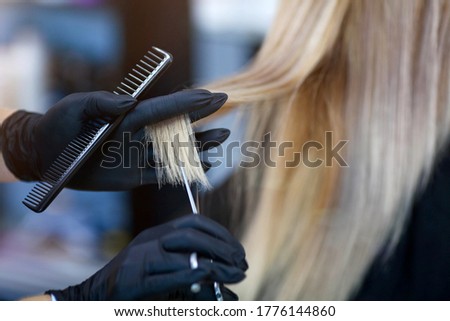 A hairdresser in rubber gloves holds a pair of scissors and a comb. Woman getting a new haircut. A hairdresser with security measures for Covid-19. Hairdressing salon opened Royalty-Free Stock Photo #1776144860
