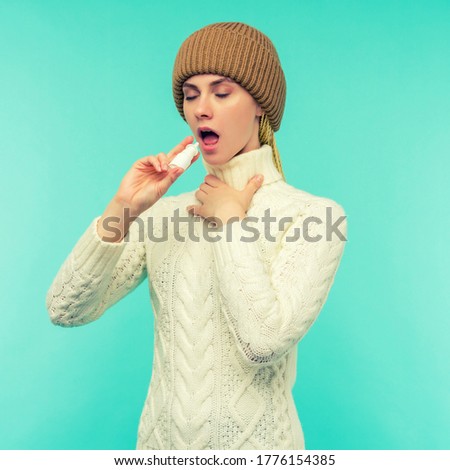 Sick young woman in scarf and hat use nasal spray isolated on blue background - image