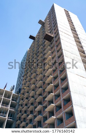 A tall house is built by a contractor with a crane. Photo of the house on a background of blue cloudless sky. Home construction, construction cranes, unfinished house