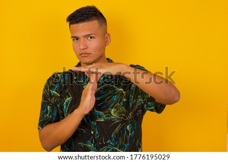Young pretty blond man tired and bored, making a timeout gesture, needs to stop because of work stress, time concept. Standing against yellow wall.