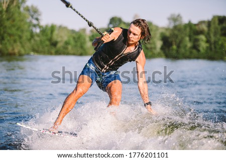 Young athletic man with long hair wakesurfing on waves of river in sunny summer weather. Ttheme outdoor activities in summer. Water sports wakesurf on the board. sliding wakeboarder in water splash.