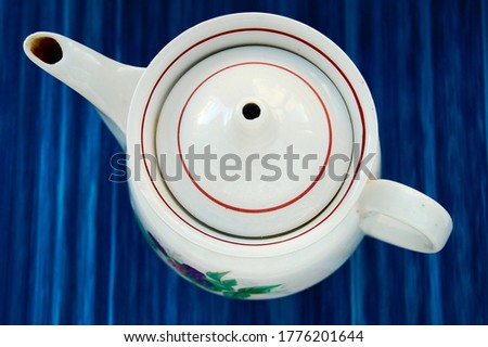 The white kettle on the blue background. The camera lacated over the kettle and on this photo you can see the top of the kettle.