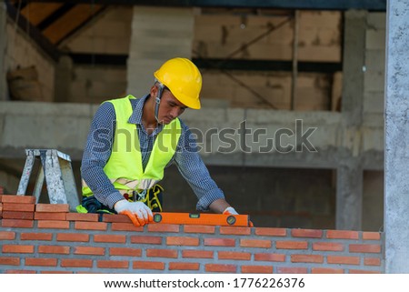 Bricklayer industrial worker installing brick masonry on exterior wall at new house.