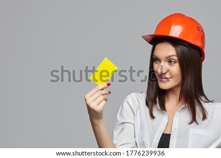 a girl in an orange construction helmet, with a business card in her hand on a white background. the concept of advertising..