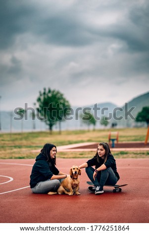 two girls and a dog sitting on the basketball court and talking