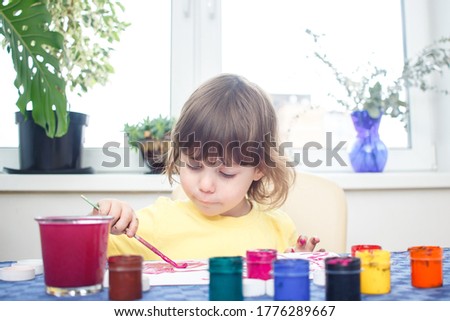 Little caucasian girl draw picture gouache in home interior during coronavirus self-isolation and quarantine. Creativity concept. Cute three year old baby is engaged in creativity.