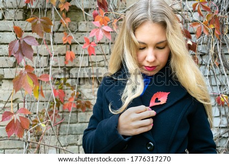 Blonde haired young woman is holding heart shaped red colored autumn leaf. Concept of waiting love, loneliness cause of breaking up or divorce
