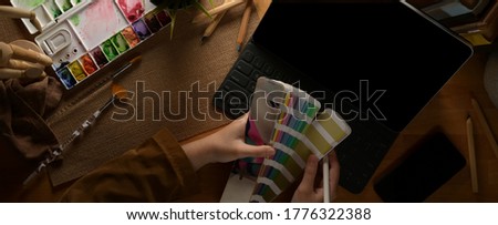 Overhead shot of female designer choosing colour on colour swatch while working with tablet on wooden table
