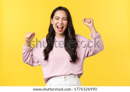 Lifestyle, emotions and advertisement concept. Happy smiling and pumped asian girl celebrating victory, chanting yes with hands raised up and broad grin, triumphing over achievement or success Royalty-Free Stock Photo #1776326990