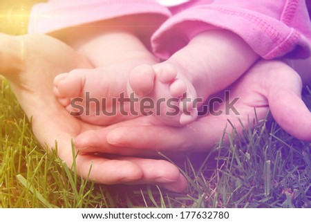 Baby feet in mother's hands outside in grass