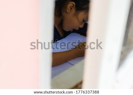 An 2-3 year-old Asian girl sitting on a window writing practice and looking out the window
