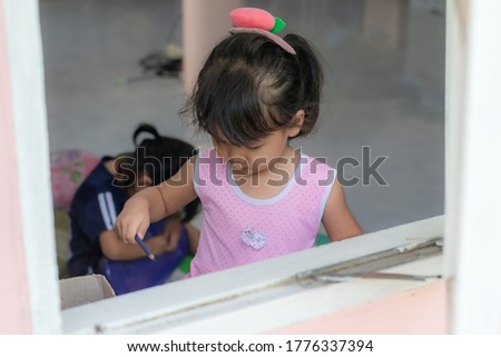 An 2-3 year-old Asian girl sitting on a window writing practice and looking out the window