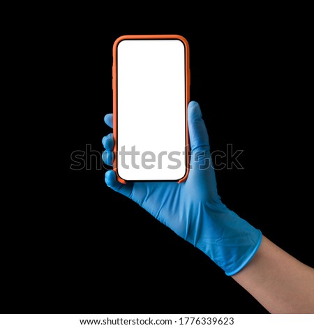 Doctor's hand in sterile medical gloves holding phone isolated on black background with clipping path. Concept of protection against pandemic and viruses.