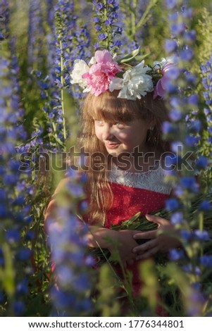 Little beautiful girl in a flower field on a sunny summer day during summer vacation. A girl with long hair smiles and laughs. Girl with a wreath on her head. Selective focus image.