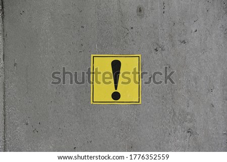 A black-and-yellow exclamation mark sticker applied to a gray metal surface