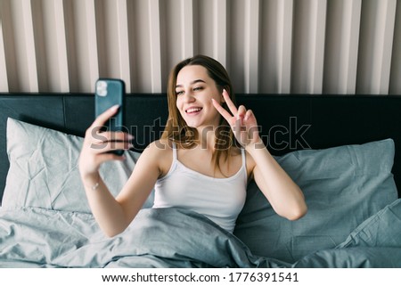 Portrait of young woman taking a selfie on bed.