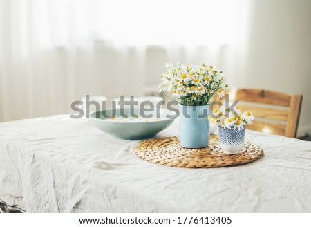 Table with flowers chamomile on linen tablecloth in living room, bright interior, Cottagecore Aesthetics Royalty-Free Stock Photo #1776413405